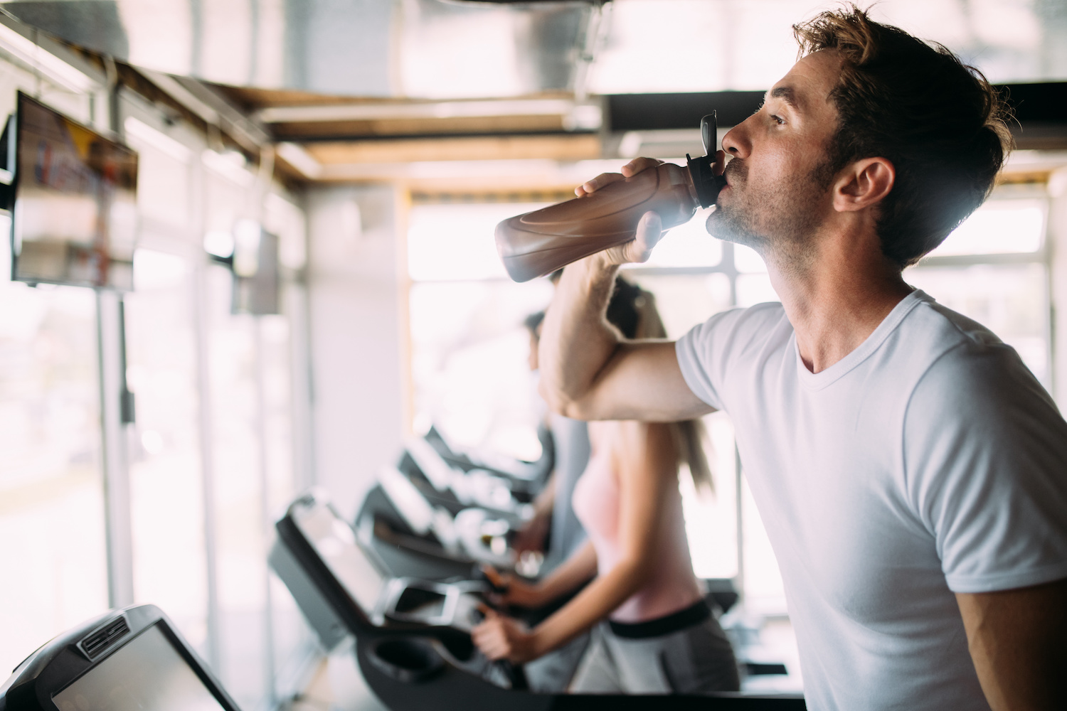 Handsome sporty fit man resting, having break drinking water after doing exercise